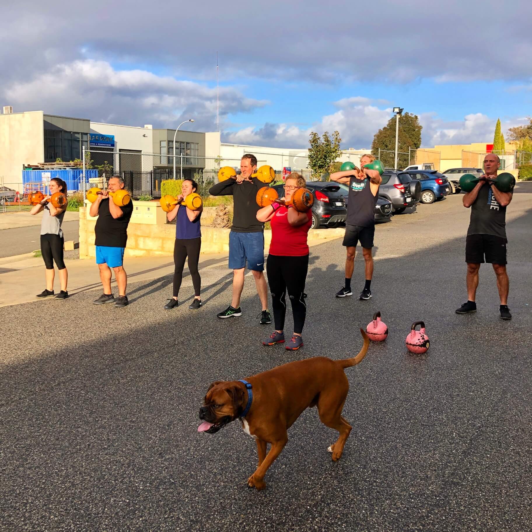 Members doing kettlebell cleans outside the gym with the gym dog