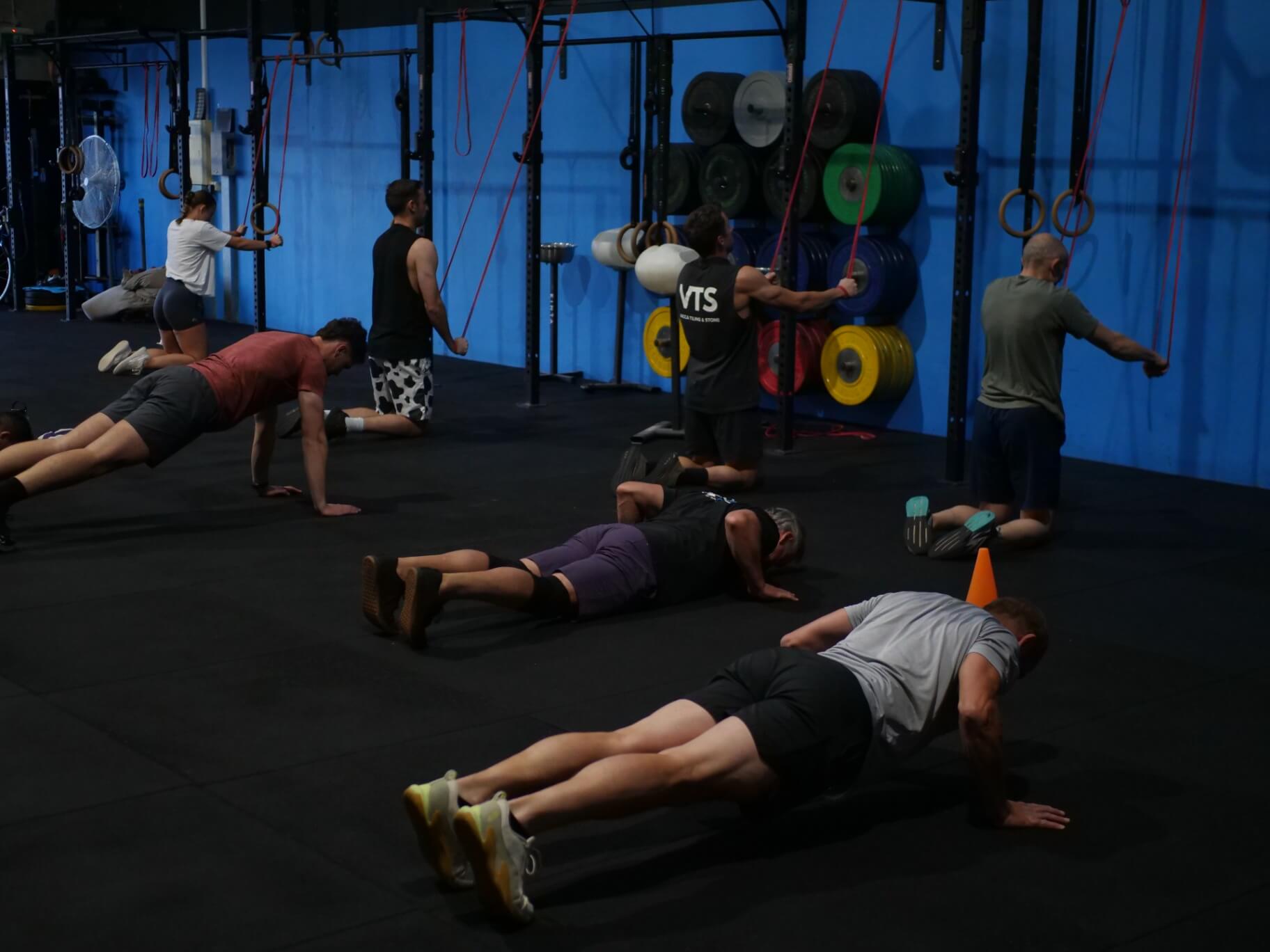 Members doing push-ups and ring rows against the blue wall
